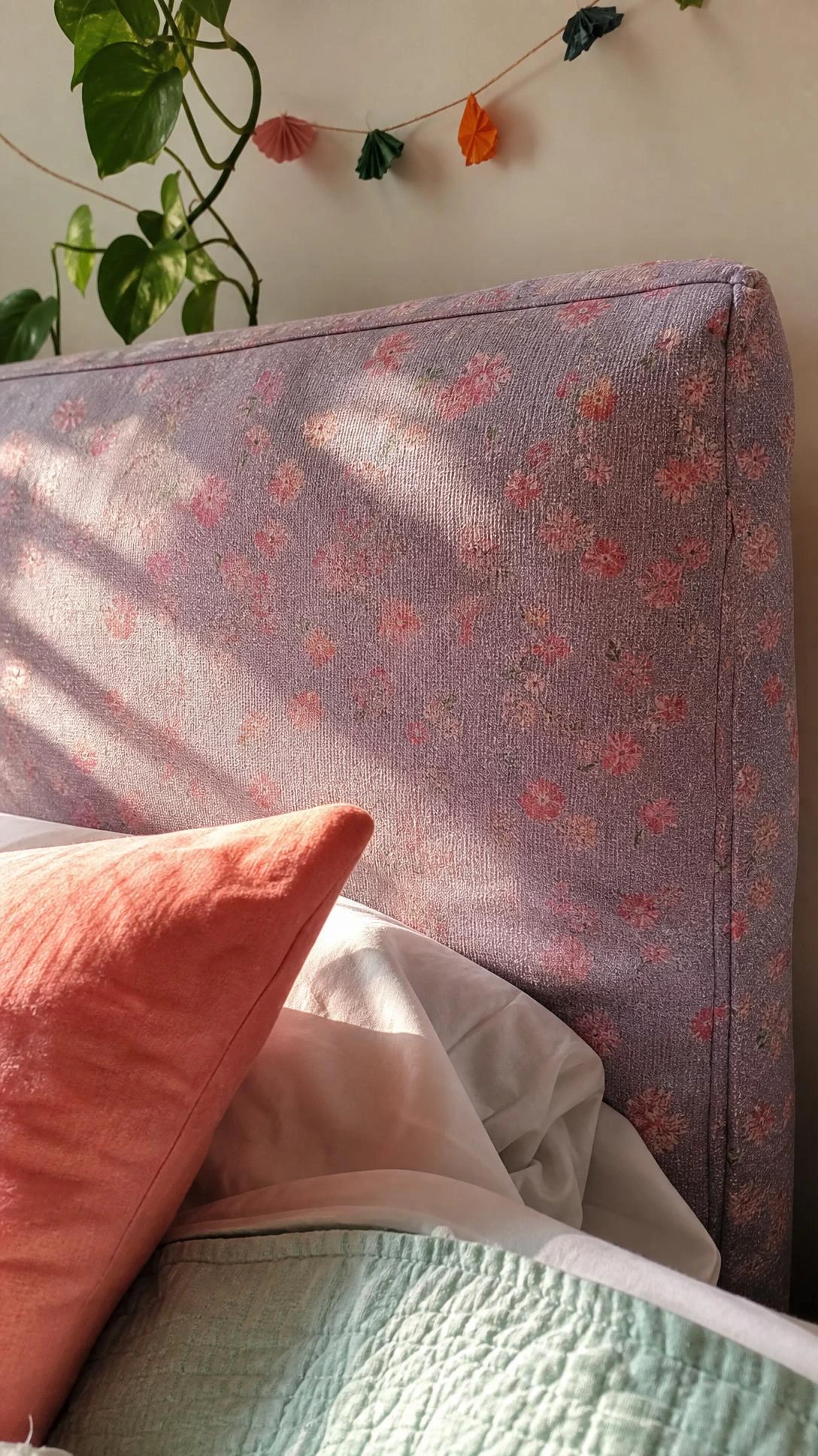Close-up of a DIY fabric headboard for a teen room, showing dusty lavender floral weave, soft padding, uneven seam, and wrinkles