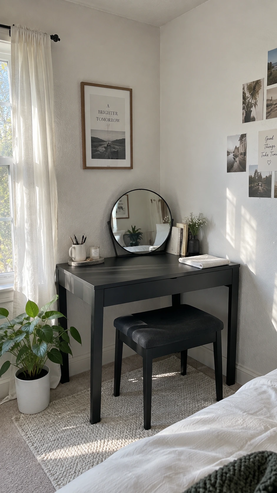 Matte black corner desk in a white bedroom with a round mirror, pen cup, and folded towel lit by natural window light