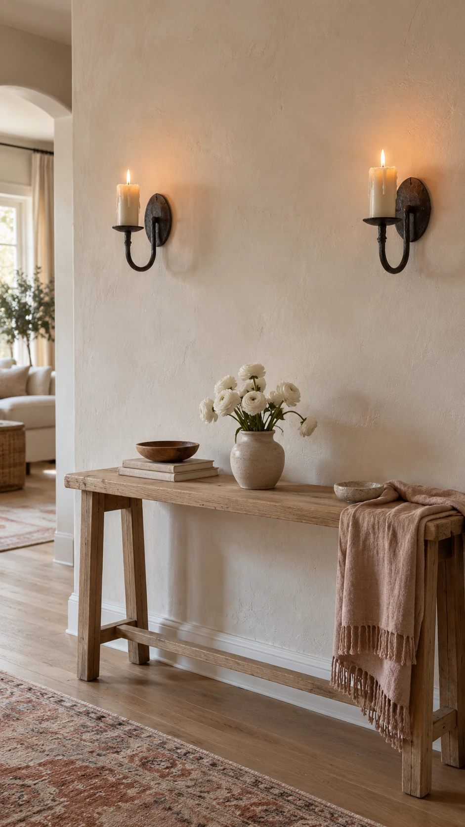 Two wrought iron hanging candle sconces mounted symmetrically on a textured off-white wall, each holding a cream pillar candle with a flickering flame for warm ambient lighting